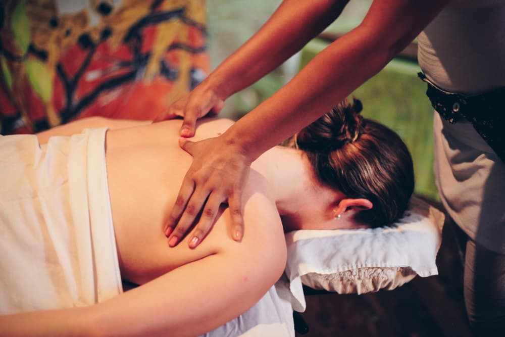 A woman lying face down on a massage table and draped in a white sheet having her back massaged