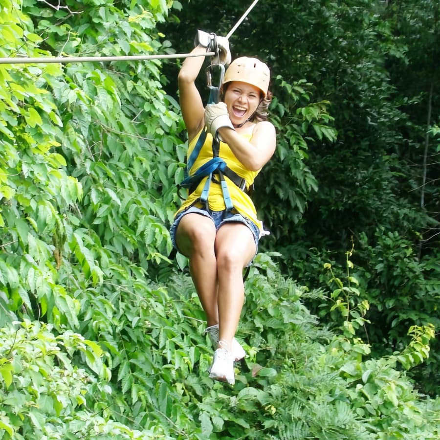 A woman with a big smile ziplining through the jungle