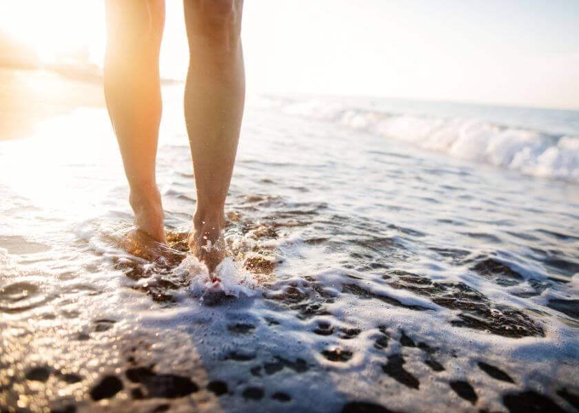 close-up of bare feet walking along the shoreline with waves washing over close-up of bare feet walking along the shoreline with waves washing over
